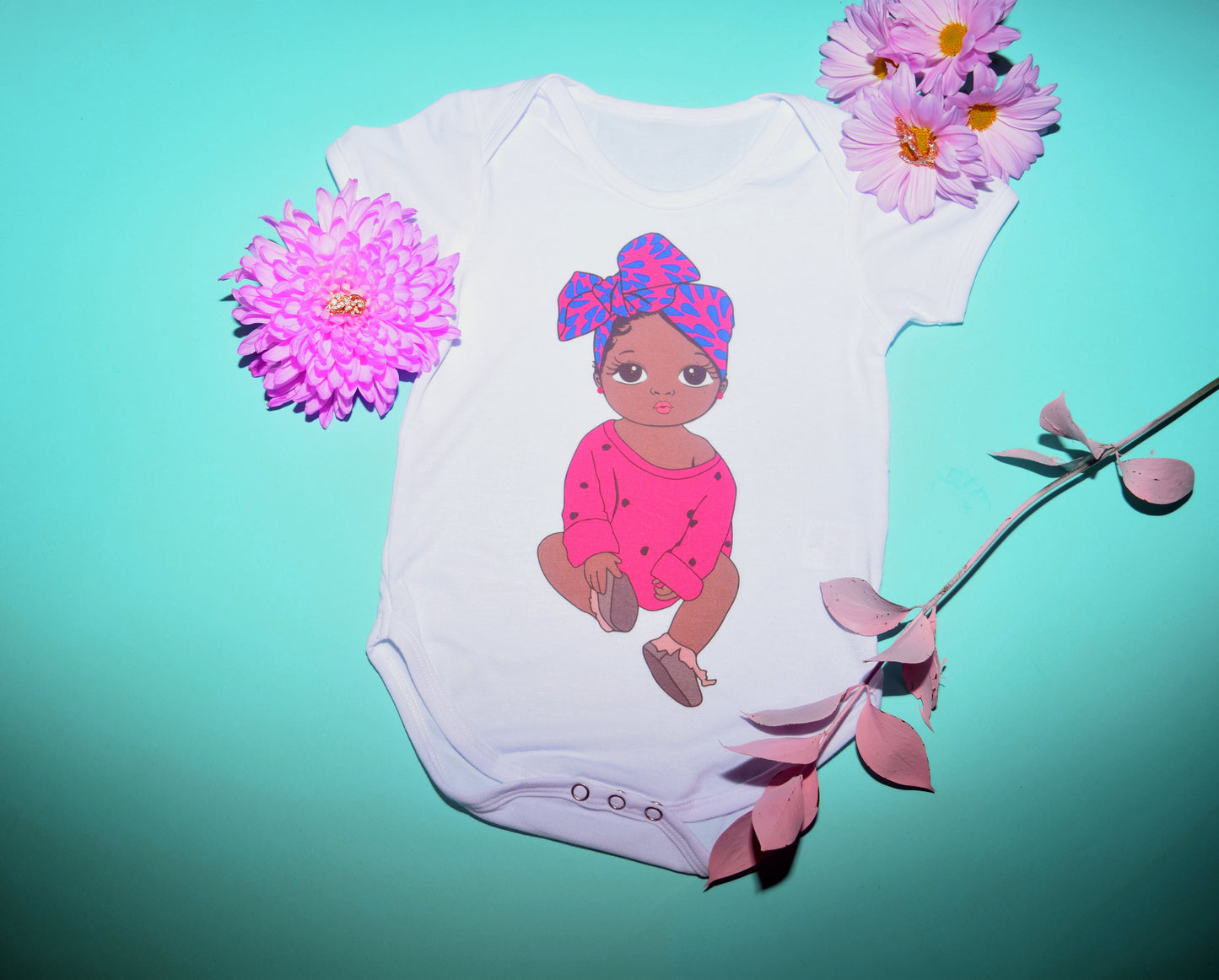 White onesie with brown baby girl wearing a turban as a protective style, and baby hairs. Little princess is wearing a pink sweater